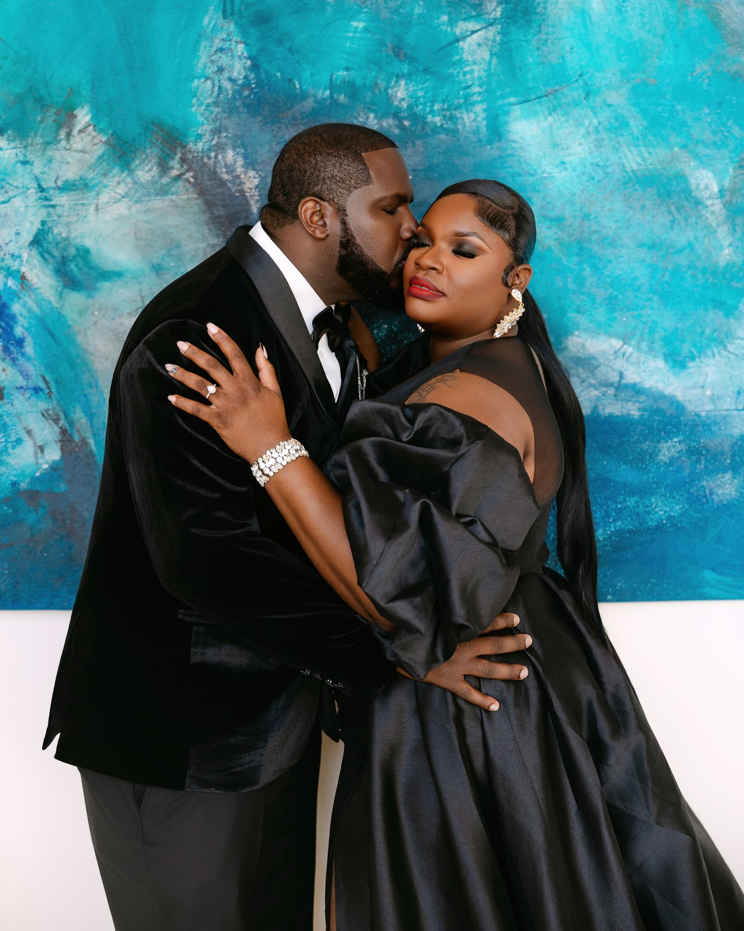 Couple embracing in black formalwear before a turquoise painting