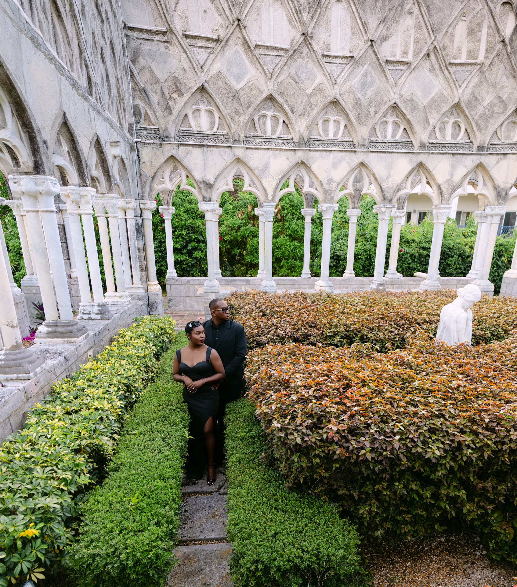 Couple in a manicured hedge garden beside gothic cloisters