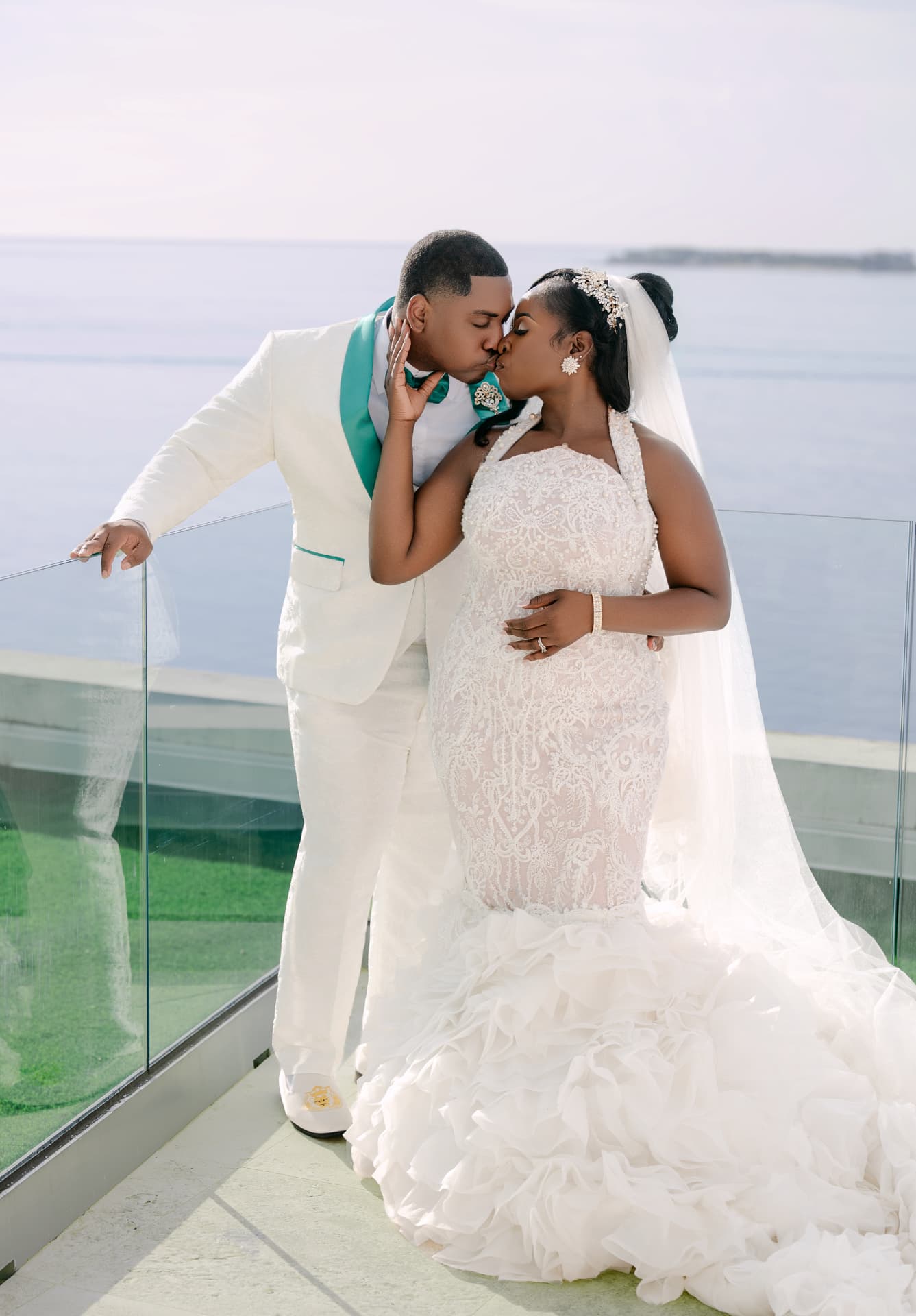 Groom kissing his bride on a glass-railed balcony above the sea