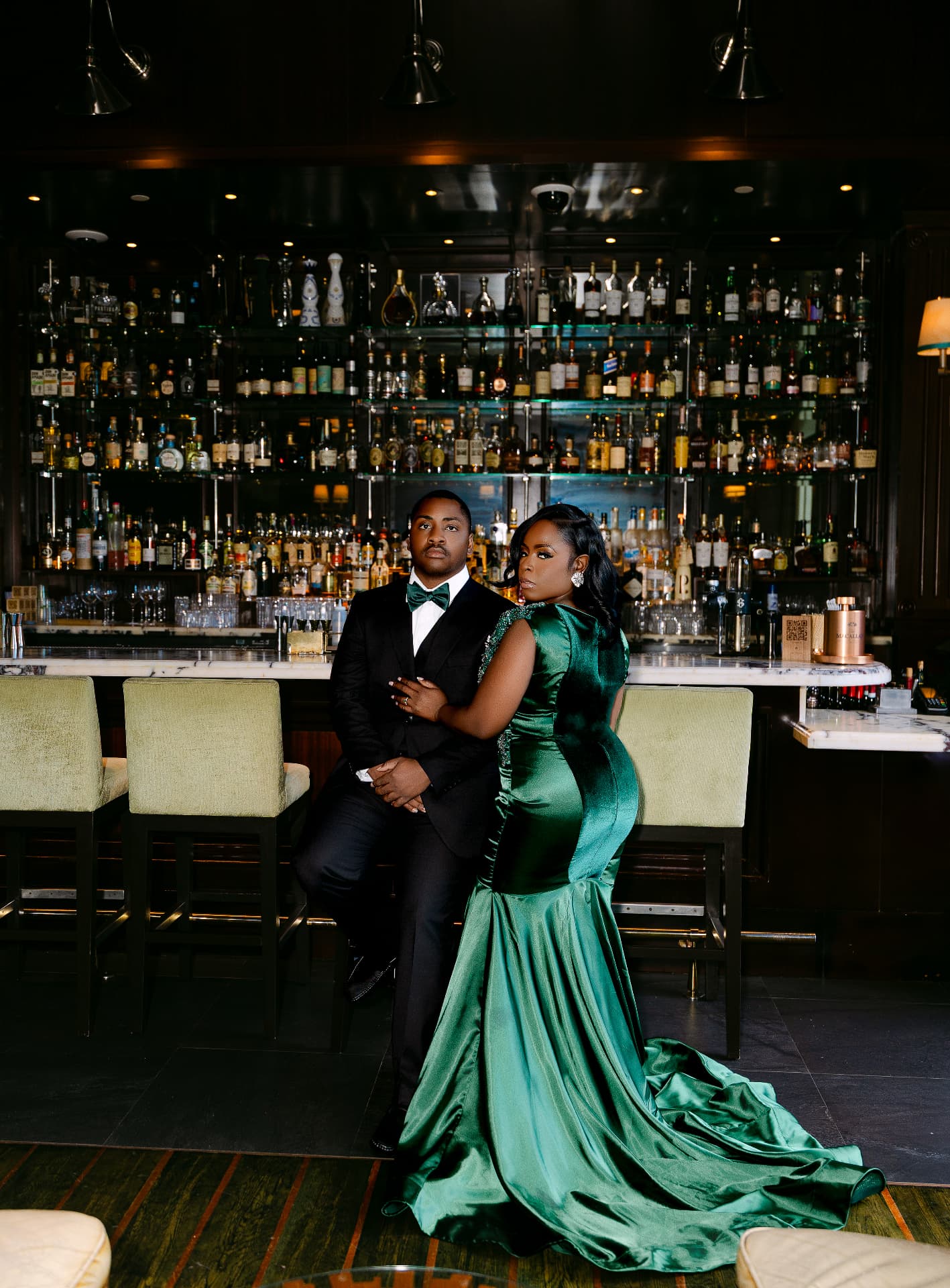 Couple in emerald and black tie at a marble cocktail bar