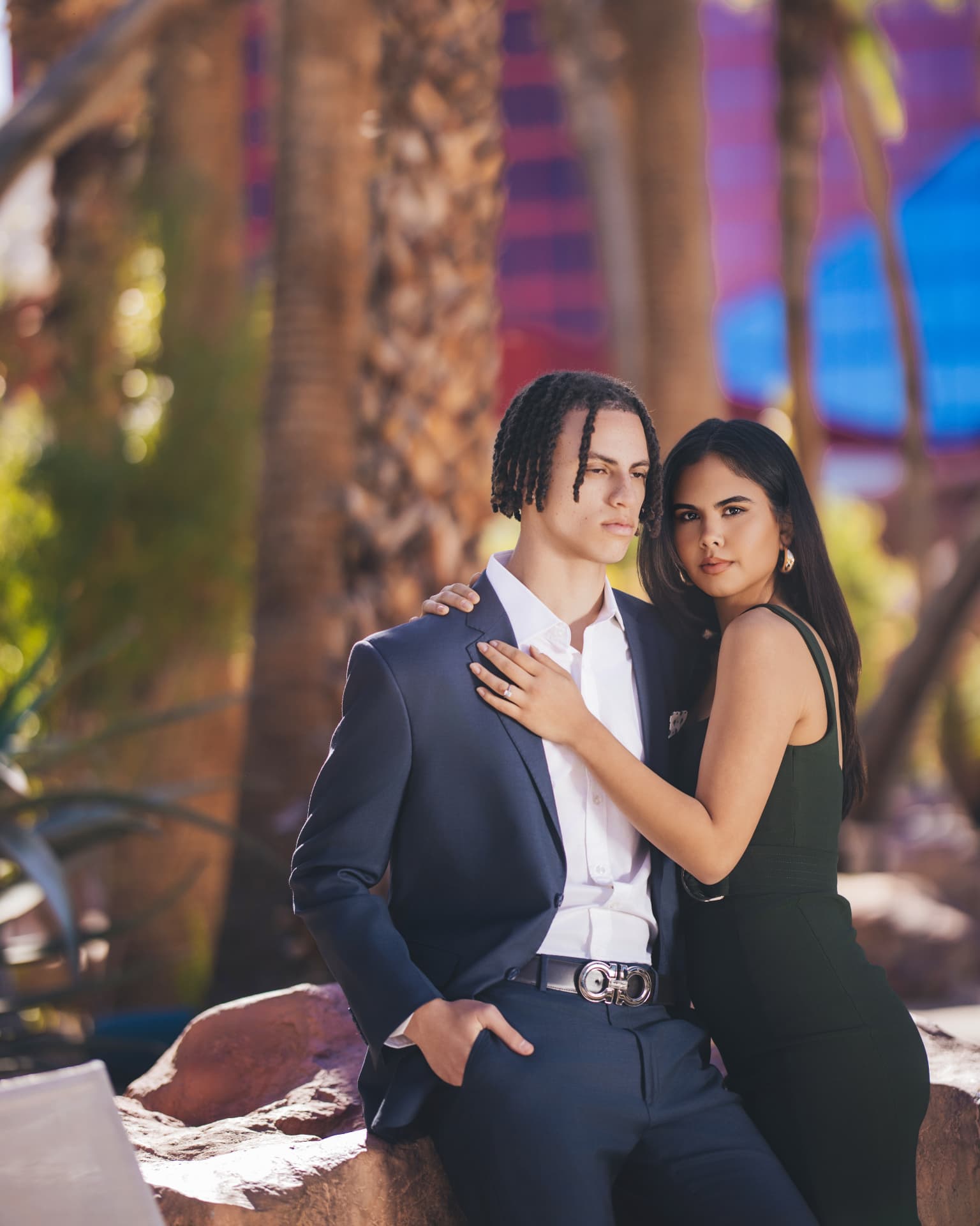 Couple in soft daylight among palms, groom in navy suit