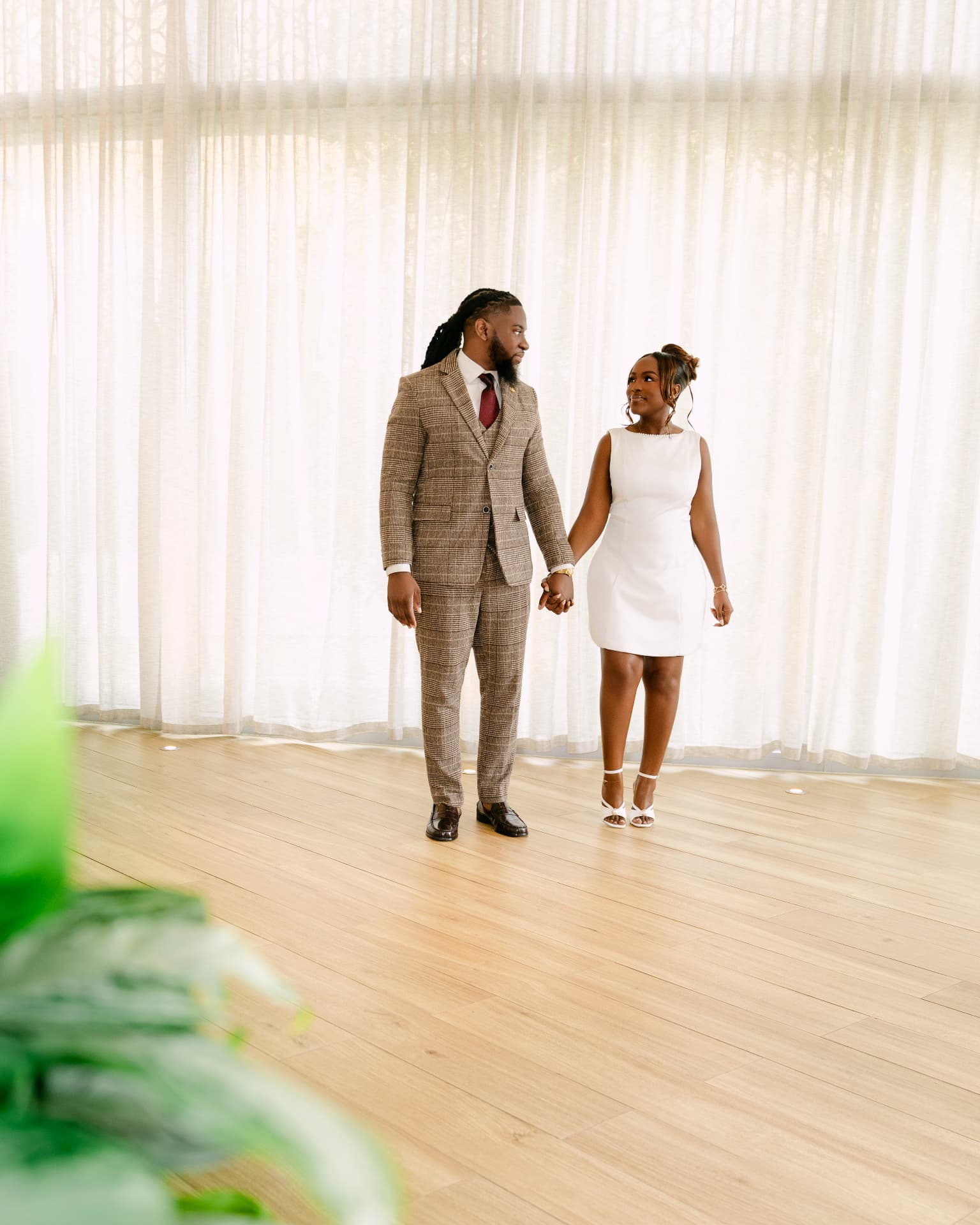 Couple holding hands in a sunlit room with sheer curtains