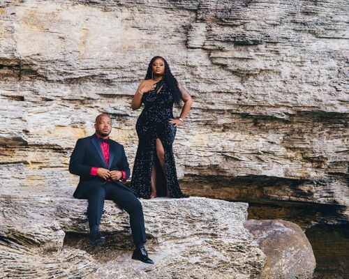Couple posing against layered rock cliffs by the sea