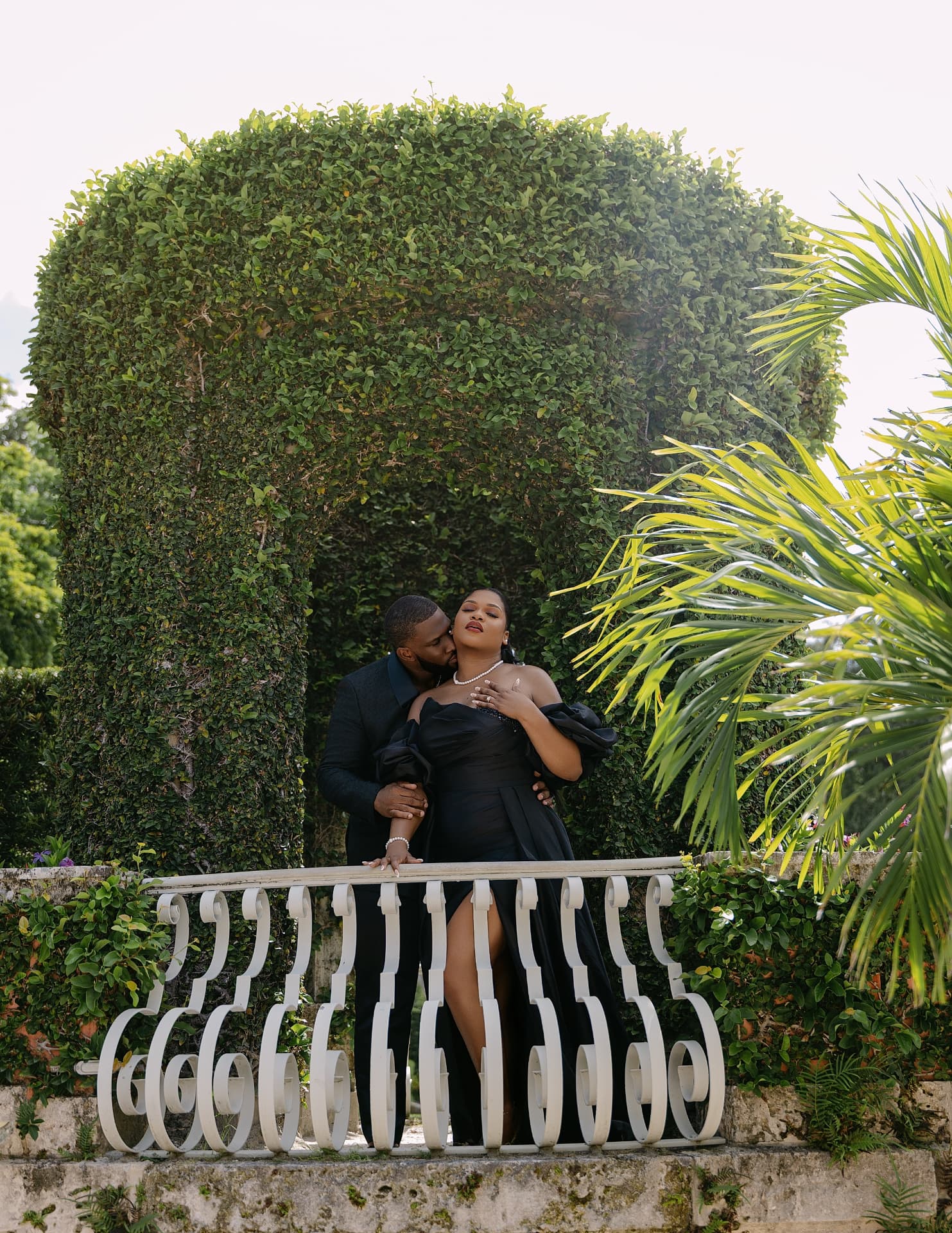 Groom kissing his fiancée’s shoulder on a garden balcony