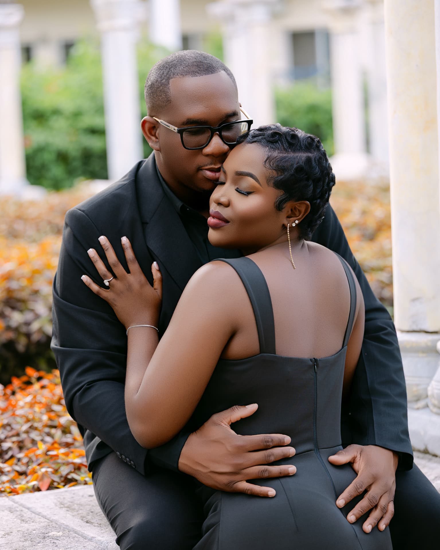 Groom kissing his fiancée’s forehead beside stone columns