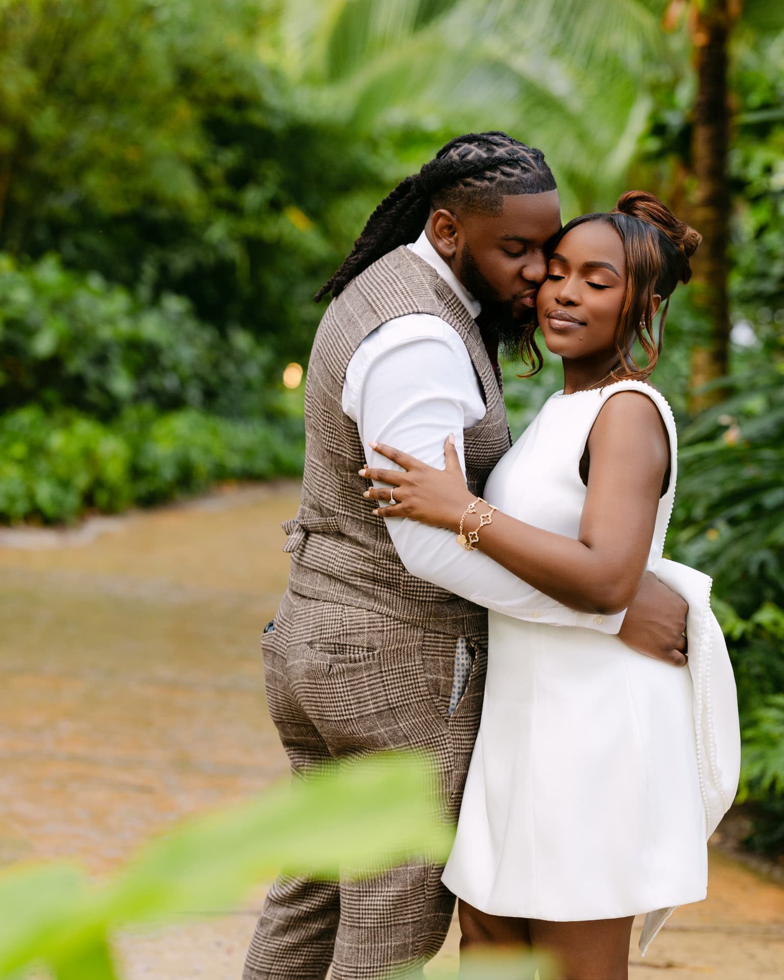 Groom kissing his fiancée’s cheek in a lush garden