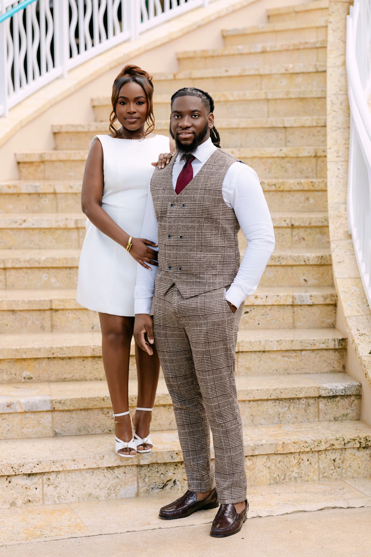 Couple on a sweeping limestone staircase in ivory and tweed