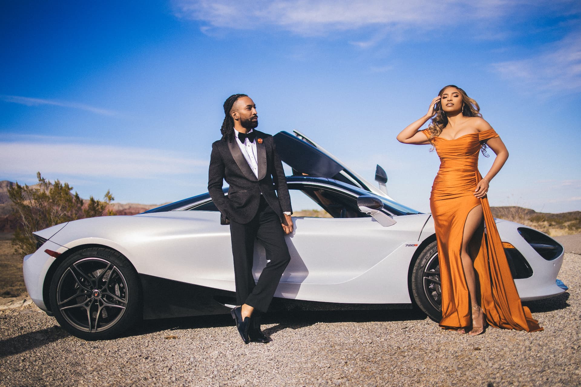 Couple in black tie beside a white supercar in the desert