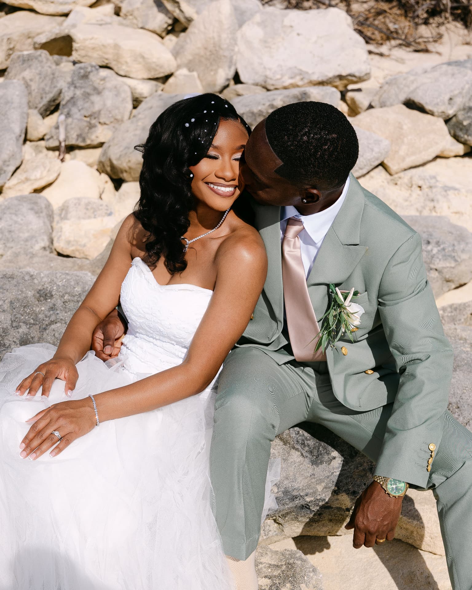 Groom kissing his bride on sunlit rocks by the shoreline